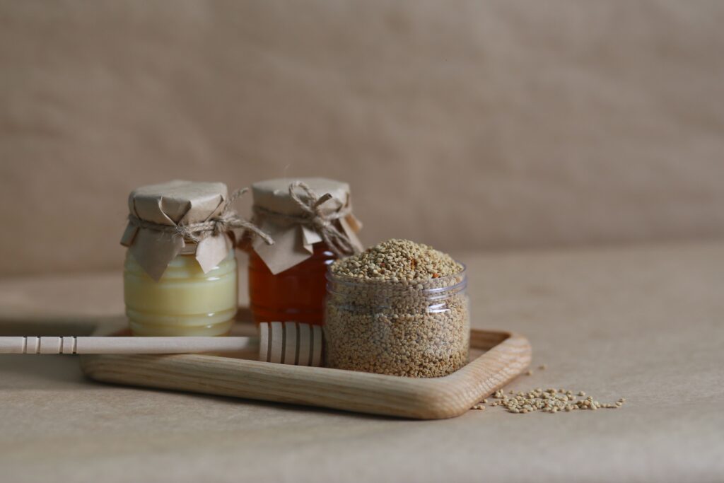 A rustic still life image featuring jars of honey and grains on a wooden tray.